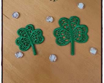 May include: Two green lace shamrock appliques on a light brown wooden surface, with six clear, round, iridescent embellishments scattered around. The initials "C&L" are in the upper right corner. The image has a border.
