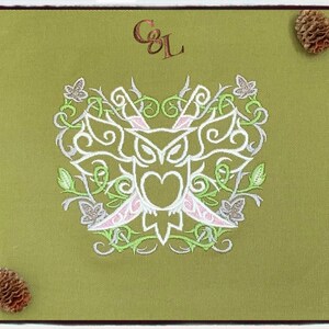 May include: Olive green canvas with an embroidered owl design in white, pink, and green. The design includes a heart shape and floral elements. The initials "C&L" are in the upper left corner. Two pinecones are in the corners.