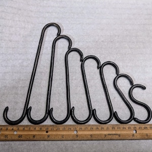 May include: Set of seven black metal S-shaped hooks of varying sizes. The hooks are arranged in a graduated pattern, with the largest hook at the top and the smallest hook at the bottom. The hooks are measured against a ruler.
