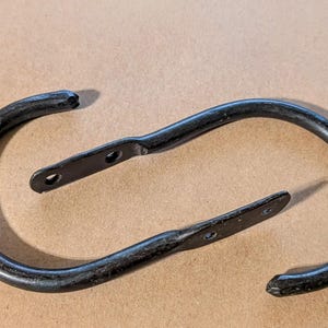 May include: Two black metal curtain rings with a simple, rounded design. The rings are made of a thick, durable metal and have a smooth, polished finish.