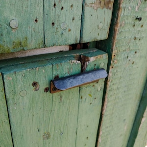 May include: A close-up of a weathered green wooden door with a metal handle. The door is made of horizontal planks and has a rustic appearance.