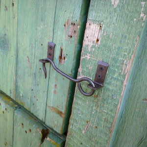 May include: A rustic, metal hook latch with a curved handle, mounted on a weathered green wooden door.