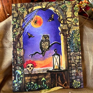 May include: A rectangular art print featuring a painted scene of an owl perched on a branch against a purple sky with a full moon, bats, and a spiderweb. A skull with red roses, a lit lantern on a table, and mushrooms are visible in the foreground.