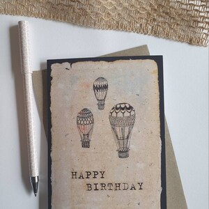 Tarjeta de feliz cumpleaños en globo aerostático anticuado por Minnie & Lou. Tinta original dibujada a mano sobre papel vintage hecho a mano reimpreso en tarjeta reciclada