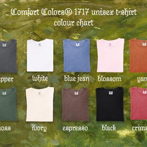 May include: Color chart of Comfort Colors 1717 unisex t-shirts. The chart displays folded t-shirts in various colors, including pepper, white, blue jean, blossom, yam, moss, ivory, espresso, black, and crimson. The text "Comfort Colors" is at the top.
