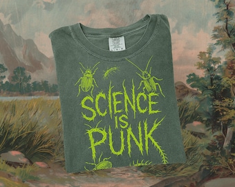Puede incluir: Una camiseta verde oscuro con el texto "SCIENCE IS PUNK" en verde brillante, junto con ilustraciones de insectos. La camiseta es de la marca Comfort Colors y el diseño está serigrafiado. La camiseta está doblada y presentada sobre un fondo pintado.