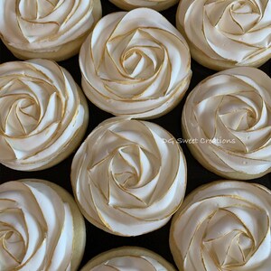 May include: Overhead shot of nine sugar cookies decorated with white frosting in a rose design, outlined with gold. The cookies are arranged closely together on a dark surface. The text "DG Sweet Creations" is visible.