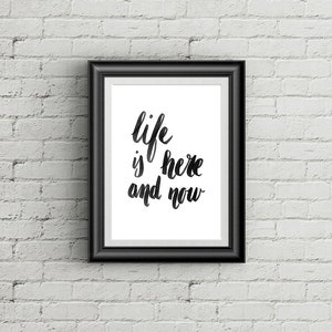 Peut inclure: Impression encadrée en noir avec un fond blanc et une calligraphie noire qui dit "life is here and now".