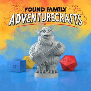 May include: A gray figurine of a furry creature holding a stringed instrument, with the text "FOUND FAMILY ADVENTURECRAFTS" above it. Blue, yellow, and red dice are in the foreground, with a colorful background.