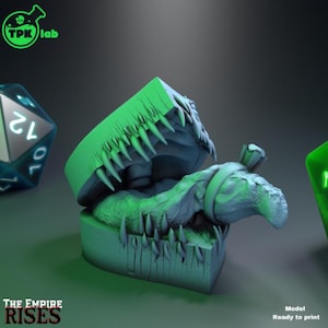 May include: A 3D-printed, green, monster-themed box with sharp teeth and a creature inside. The box is open, revealing the detailed interior. The text "THE EMPIRE RISES" is visible. The image also includes a green and a blue die.