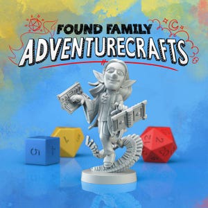 May include: A gray figurine of a smiling elf-like character holding two rectangular objects, with the text "FOUND FAMILY ADVENTURECRAFTS" above. Three colorful dice are in the background: blue, yellow, and red.
