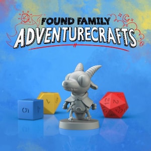 May include: A gray figurine of a goat-like creature with large eyes and horns, wearing a cape, stands on a circular base. The image includes a blue, yellow, and red dice, and the text "FOUND FAMILY ADVENTURECRAFTS" in a playful font.