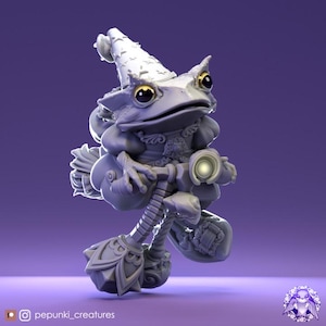 Puede incluir: Una figura caprichosa de una rana mago, sosteniendo una escoba y un orbe brillante. La rana lleva un sombrero puntiagudo con detalles de estrellas y un atuendo decorativo. La figura es de color gris claro sobre un fondo púrpura.