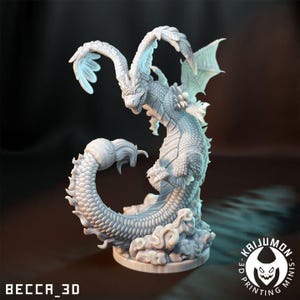 May include: A detailed, white dragon figurine with a serpentine body, large wings, and a detailed head. The dragon is posed on a cloud-like base. The text "BECCA_3D" and a logo for "KAIJUMON MINIS" are visible.