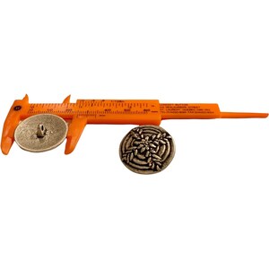 May include: A close-up of a silver metal button with a decorative design. The button is being measured with a caliper, showing it is 1.2 cm in diameter.