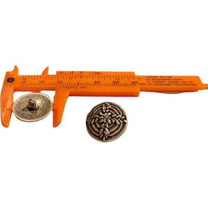 May include: A silver-toned button with a snowflake design, measured with a ruler. The button is 1.5 cm in diameter.