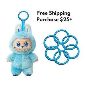 May include: A light blue plush monster toy with a matching keychain and six blue key rings. The monster has a smiling face with blue eyes and a hood. The keychain has the text "THE MONSTER".