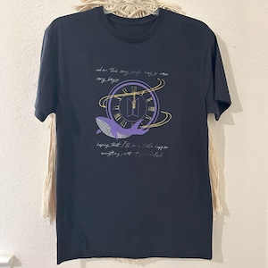 May include: Black t-shirt with a purple whale graphic and the text "when this song ends, may a new song begin" and "hoping that I'll be a little happier everything just to be ok". The graphic includes a clock design with the BTS logo.