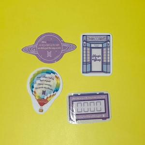 May include: A collection of stickers on a yellow background. The stickers include a purple planet with text, a blue and white shop, a colorful hot air balloon, and a digital clock with text. The stickers have text in English.