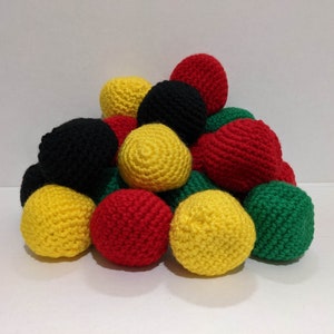 May include: A collection of crocheted balls in red, yellow, black, and green colors. The balls are arranged in a pyramid shape.