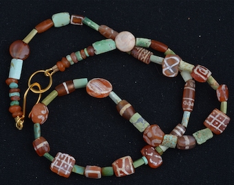 May include: A necklace featuring a variety of beads in shades of red, brown, green, and white. The beads are of various shapes, including round, oval, and rectangular. The necklace is fastened with a gold-colored clasp.