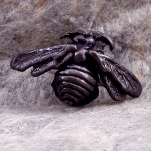 May include: A small, detailed, black metal bee figurine. The bee has a segmented body and wings.