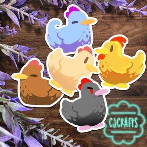 May include: A collection of five colorful chicken stickers. The stickers feature chickens in various colors, including blue, yellow, brown, beige, and gray, each with a red comb and yellow beak. The stickers are on a wooden background with purple flowers and the text "CJ CRAFTS".