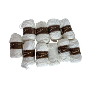 May include: A collection of white yarn skeins, each wrapped with a brown label. The yarn is arranged on a white surface. The labels have text that is difficult to read.