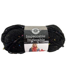 May include: A skein of black yarn with colorful flecks. The label reads "Loops & Threads Impeccable". The yarn is tightly wound and appears soft, suitable for knitting or crochet projects. The image shows a close-up of the yarn.