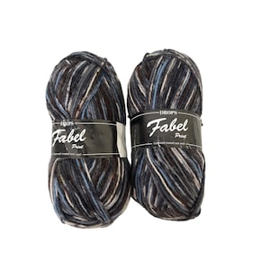 May include: Two skeins of Drops Fabel Print superwash treated sock wool yarn. The yarn is a mix of dark gray, brown, light blue, and white. Each skein has a black label with white text.