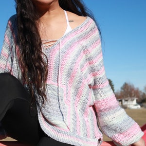 May include: A striped crochet sweater with pink, white, and gray stripes. The sweater has a V-neck and long sleeves.