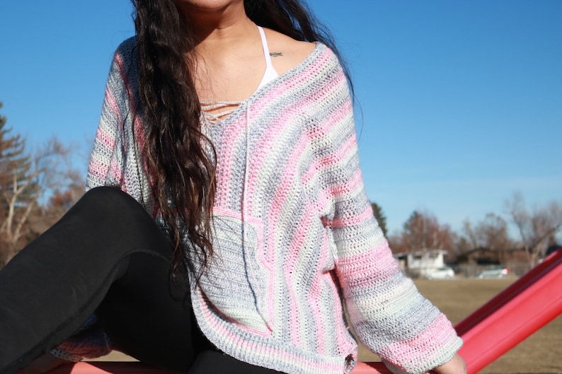 May include: A striped crochet sweater with pink, white, and gray stripes. The sweater has a V-neck and long sleeves.