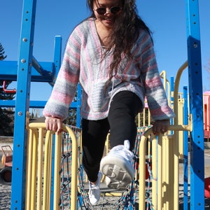 May include: A young person wearing a pink and white striped sweater and black pants is climbing on a yellow and blue playground structure. The person is wearing sunglasses and white sneakers.