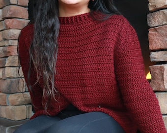 May include: A woman wearing a maroon crocheted sweater and black leggings. She is sitting on a stone ledge in front of a fireplace.