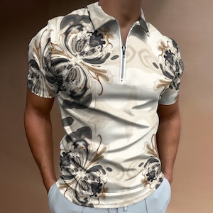 Puede incluir: Una camisa blanca de manga corta con cuello, cierre de cremallera y estampado floral abstracto marrón y negro.