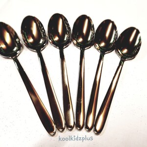 May include: Six silver spoons arranged in a fan shape on a white surface.