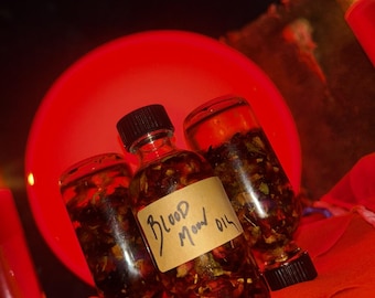 May include: Three glass bottles filled with a dark liquid and botanicals, labelled "Blood Moon Oil" in handwritten script. The bottles have black caps and are set on a red surface, with a large red orb in the background.