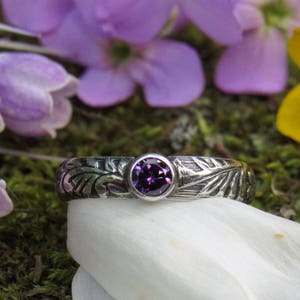 May include: A silver ring with an intricate design and a purple gemstone in the center.