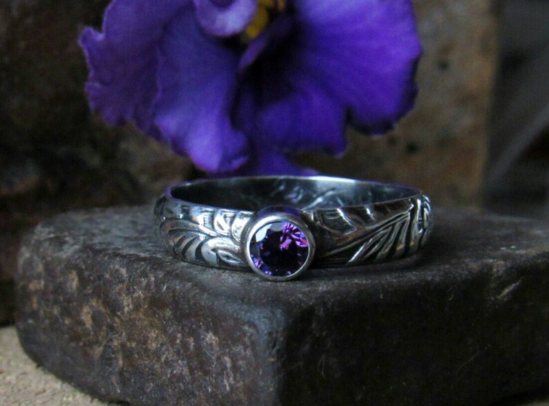 May include: A silver ring with an intricate floral design and a purple amethyst gemstone.