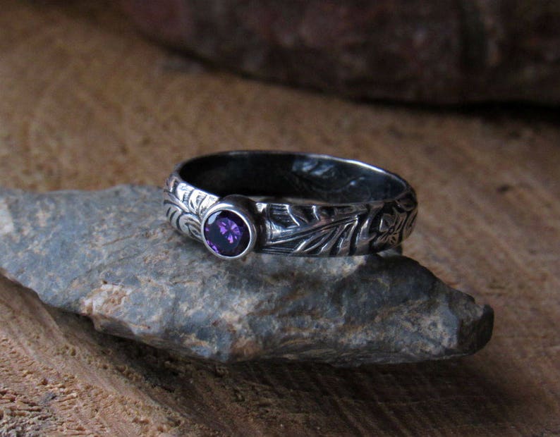 May include: A silver ring with an intricate floral design and a purple gemstone.