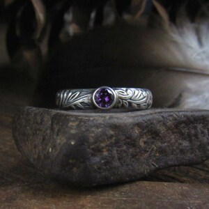 May include: A silver ring with a purple gemstone set in a floral design.