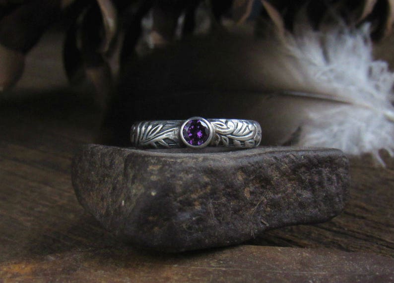 May include: A silver ring with a purple gemstone set in a floral design.