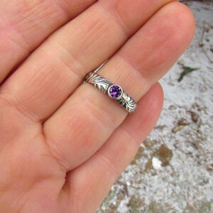 May include: A silver ring with a purple gemstone set in a floral design.