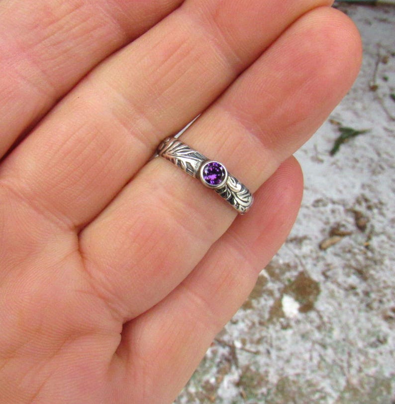 May include: A silver ring with a purple gemstone set in a floral design.