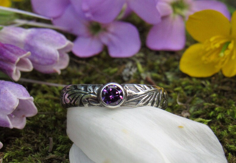 May include: A silver ring with an intricate design and a purple gemstone in the center.