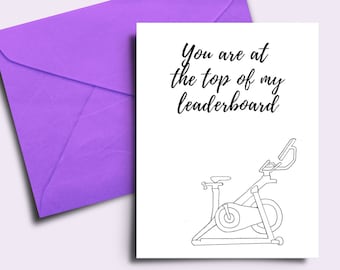 May include: A greeting card with a purple envelope. The card has the text "You are at the top of my leaderboard" above a line drawing of a stationary exercise bike. The background is a light purple.