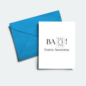 May include: A white greeting card with the text "BA! You're Awesome" and a blue envelope. The card features a stylized design within a square. The text is in a simple, modern font.