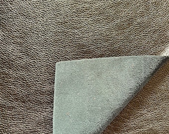 May include: A piece of brown leather with a textured surface. The leather is folded over to reveal a dark green fabric lining.