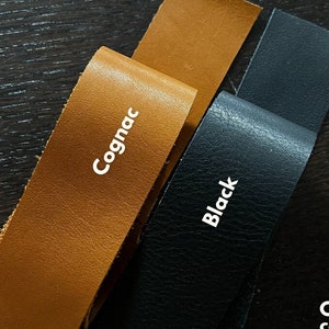 May include: Two leather strips, one cognac brown and one black, with the text "Cognac" and "Black" printed on them. The text "Craft with convenience" is printed below the strips, along with the text "Our Loved Leathers available in 1.5 inch Pre Cut strips".