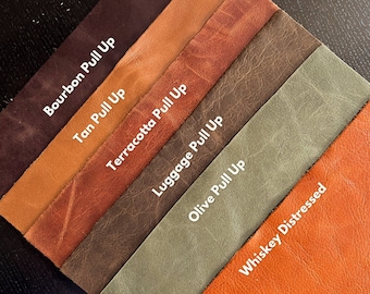 May include: Six leather swatches in different colors and finishes, including Bourbon Pull Up, Tan Pull Up, Terracotta Pull Up, Luggage Pull Up, Olive Pull Up, and Whiskey Distressed. The swatches are arranged in a staggered pattern, with the darkest color at the top and the lightest color at the bottom. The text "Craft Smaller Dream Bigger" is printed on the bottom left corner of the image. The text "Our Loved Distressed Leathers available in 8.5" by 11" Pre Cut Pieces" is printed on the bottom right corner of the image.